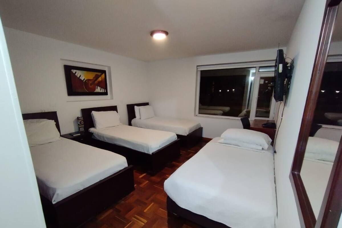 A hotel room with three single beds, a wooden floor, a large window, and a painting on the wall.