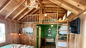 Una cabaña acogedora de madera con un dormitorio en el altillo, una zona de cocina y un comedor.