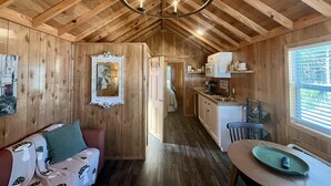 A cozy cabin interior with a wooden ceiling, a dining area, a kitchen with a microwave, and a hallway leading to a door.