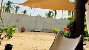 A covered outdoor seating area with a chair and a table, a concrete wall, and a sandy ground.