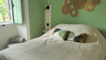 A bedroom with a large bed, a window with green shutters, a wall-mounted air conditioner, and decorative wall art.