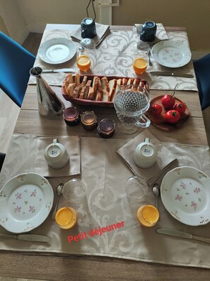 Mesa de comedor dispuesta para dos personas, con platos, vasos, una cesta de pan y condimentos.