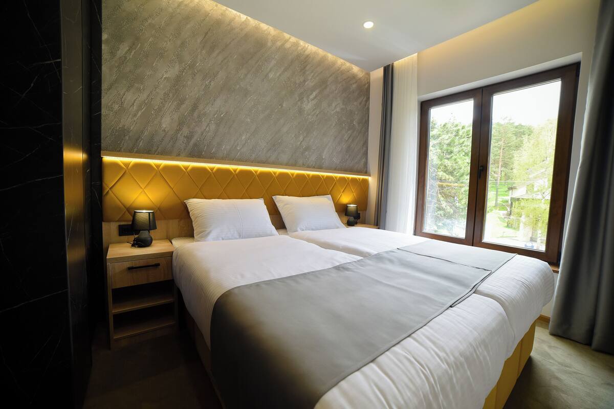 A double bed with a headboard, bedside tables, and a window with curtains.