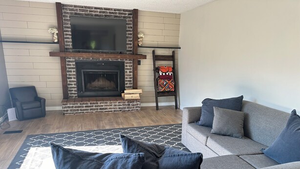 A living room with a fireplace, grey sofa, patterned rug, and a small wooden shelf with decorative items. - Large newly renovated house.  Cozy and convenient.  (Valemount)