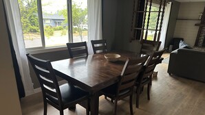 A dining area with a wooden table and chairs, a basket on the table, and a view of the outside through large windows. - Large newly renovated house.  Cozy and convenient.  (Valemount)