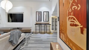 Una sala de estar moderna con un televisor grande, un sofá, una mesa de centro y una zona de bar con taburetes.