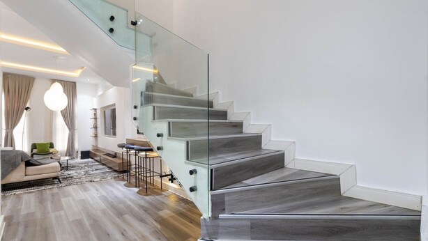 Un interior moderno con una escalera, piso de madera y barandilla de vidrio.