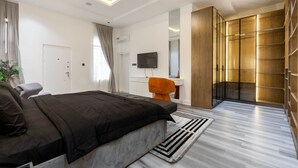 Un dormitorio moderno con una cama grande, un escritorio, un televisor y un vestidor.