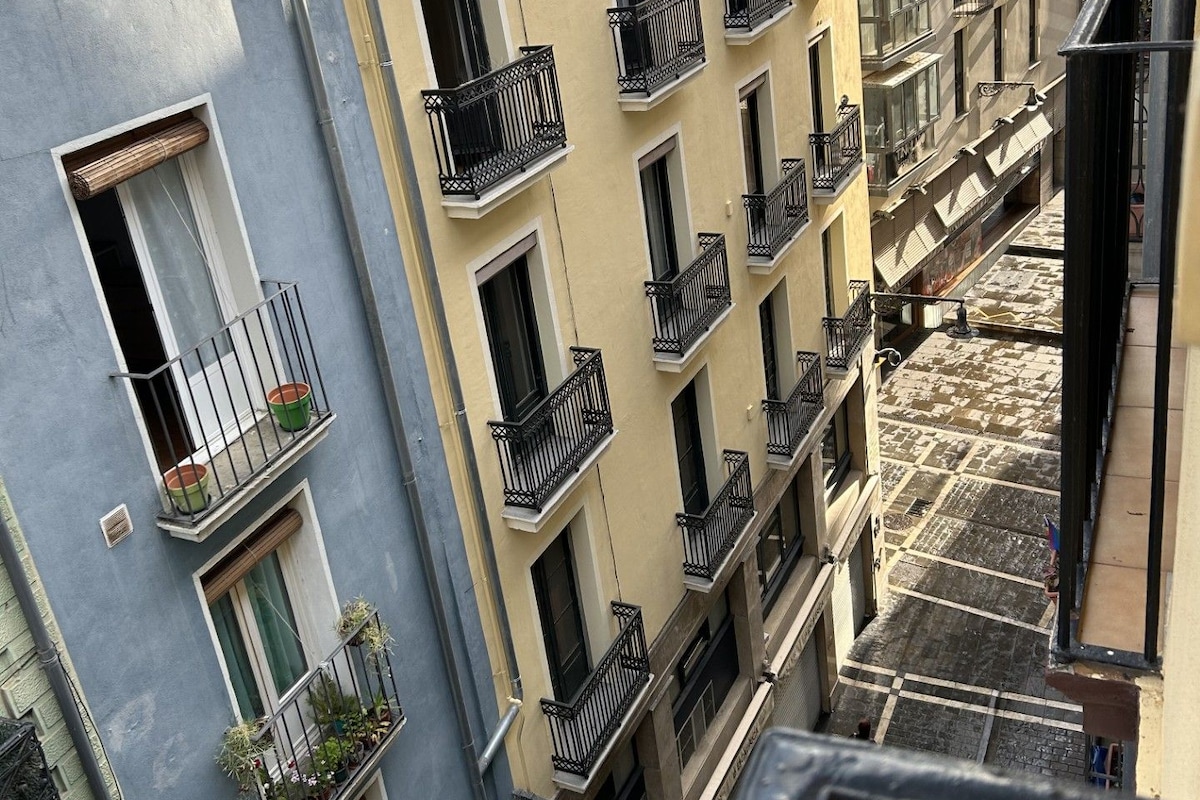 A multi-story building with balconies, a staircase, and a narrow street.