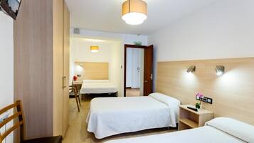 Habitación de hotel con dos camas, cabecera de madera, mesita de noche con lámpara y un pequeño escritorio con una planta.