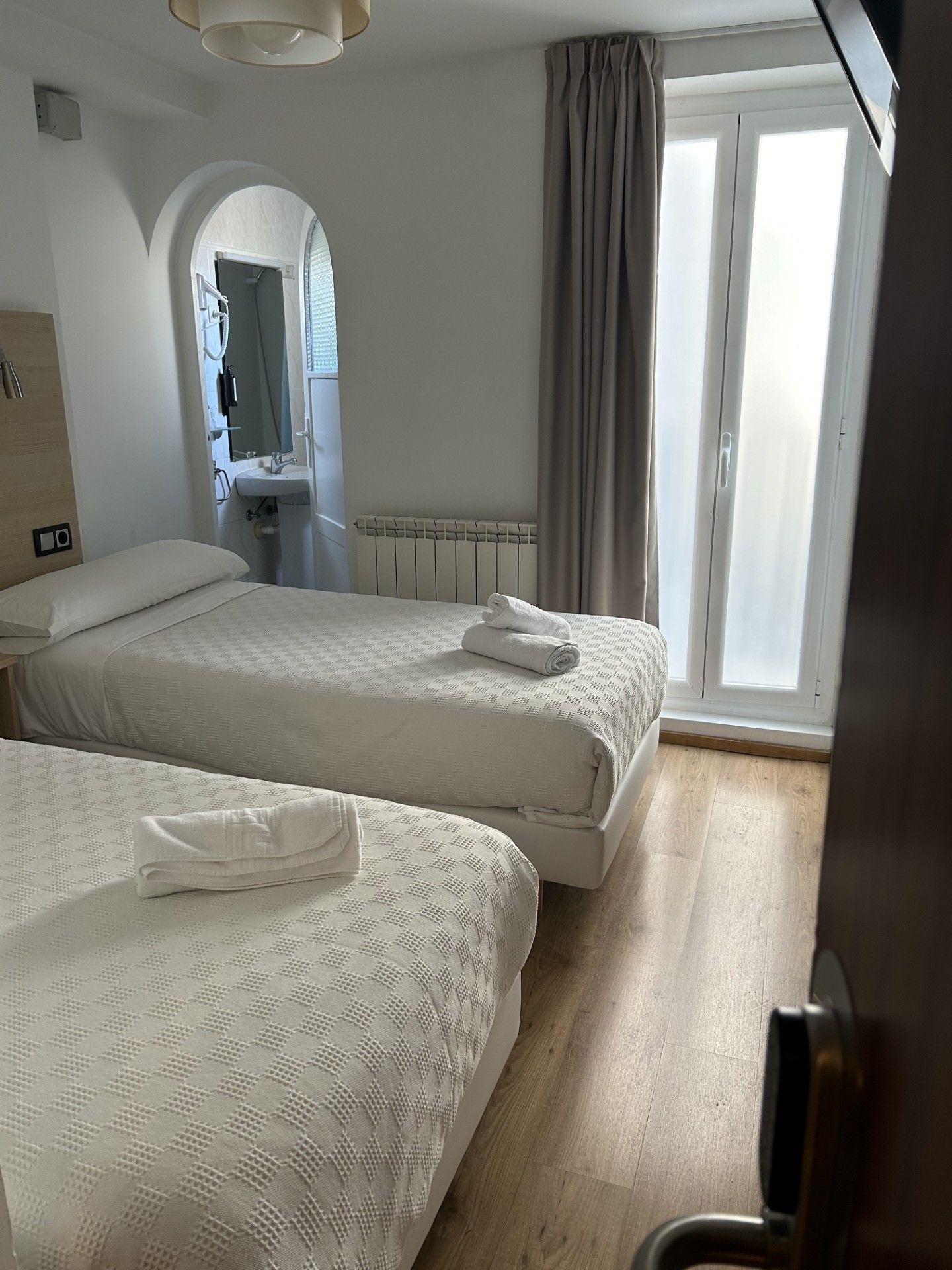 A hotel room with two beds, a bathroom, and a view of the outside.