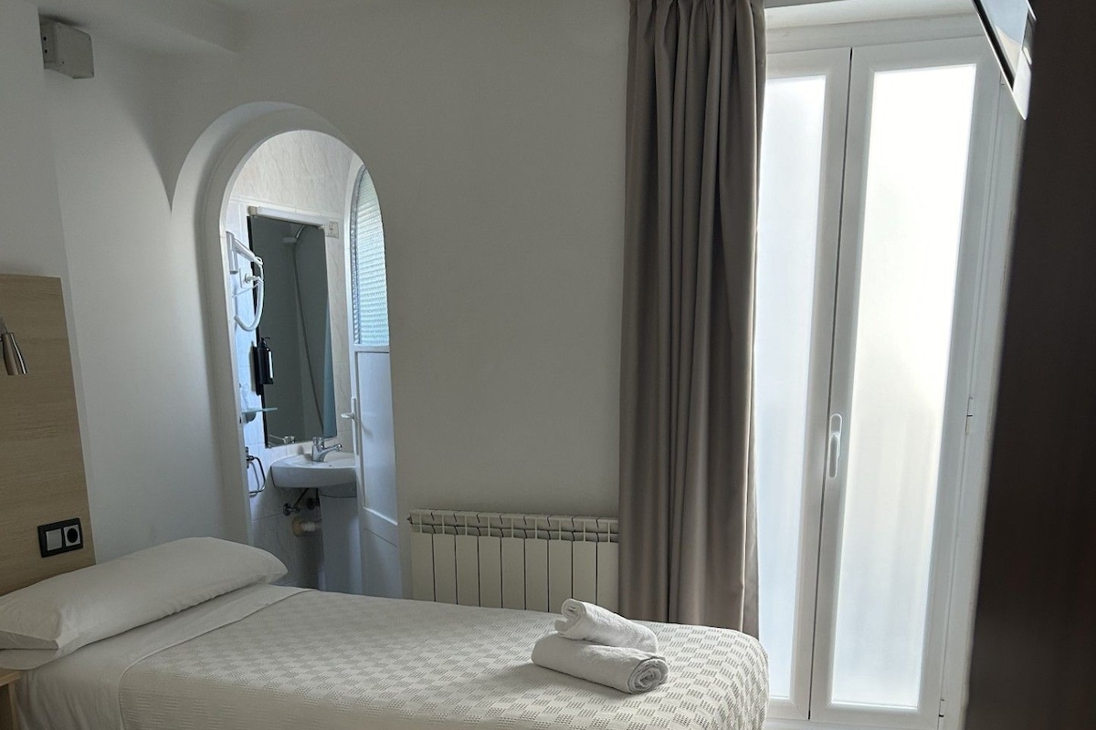 A hotel room with two beds, a bathroom, and a view of the outside.