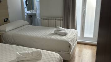 A hotel room with two beds, a bathroom, and a view of the outside.
