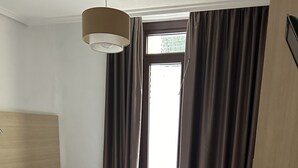 A neatly arranged hotel room with a large bed, a bedside table, a small round table, and a window with curtains. - Casa Otano (Pamplona)