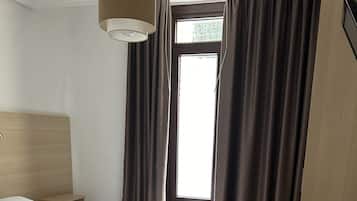 Ein ordentlich eingerichtetes Hotelzimmer mit einem großen Bett, einem Nachttisch, einem kleinen runden Tisch und einem Fenster mit Vorhängen.