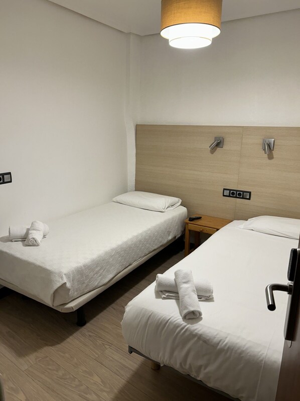 A hotel room with two single beds, each with a wooden headboard, white linens, and a small wooden nightstand. - Casa Otano (Pamplona)