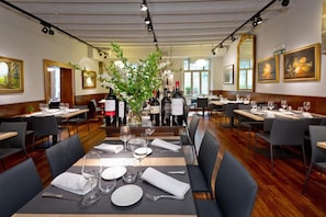 A restaurant with multiple tables set for dining, featuring a central floral arrangement and wine bottles on the tables. - Casa Otano (Pamplona)
