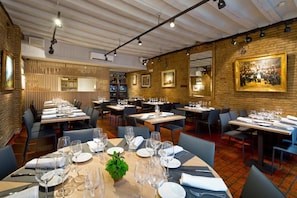 A restaurant with multiple tables set for dining, featuring a brick wall and wooden paneling. - Casa Otano (Pamplona)