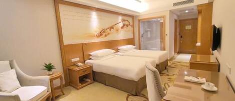 A hotel room with a bed, a desk, a chair, a nightstand, a small table with a plant, and a wall-mounted TV.