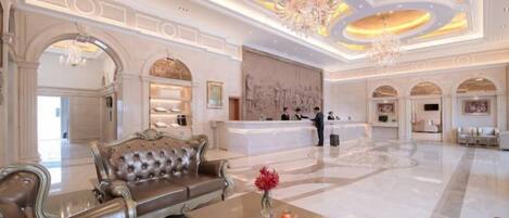 A spacious lobby with a reception desk, a leather sofa, and a chandelier.