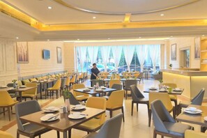 Spisested i et hotel med flere borde og stole, en disk samt udsigt til det fri.
