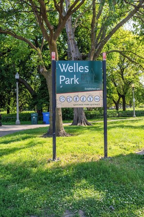 A sign for Welles Park with a tree and grass in the background.