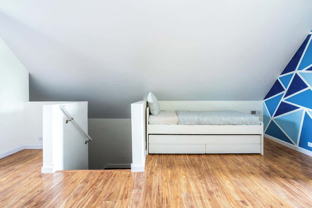 Ein kleiner, moderner Raum mit einem weißen Bett, einem weißen Kleiderschrank und einer Wand mit geometrischen Mustern.