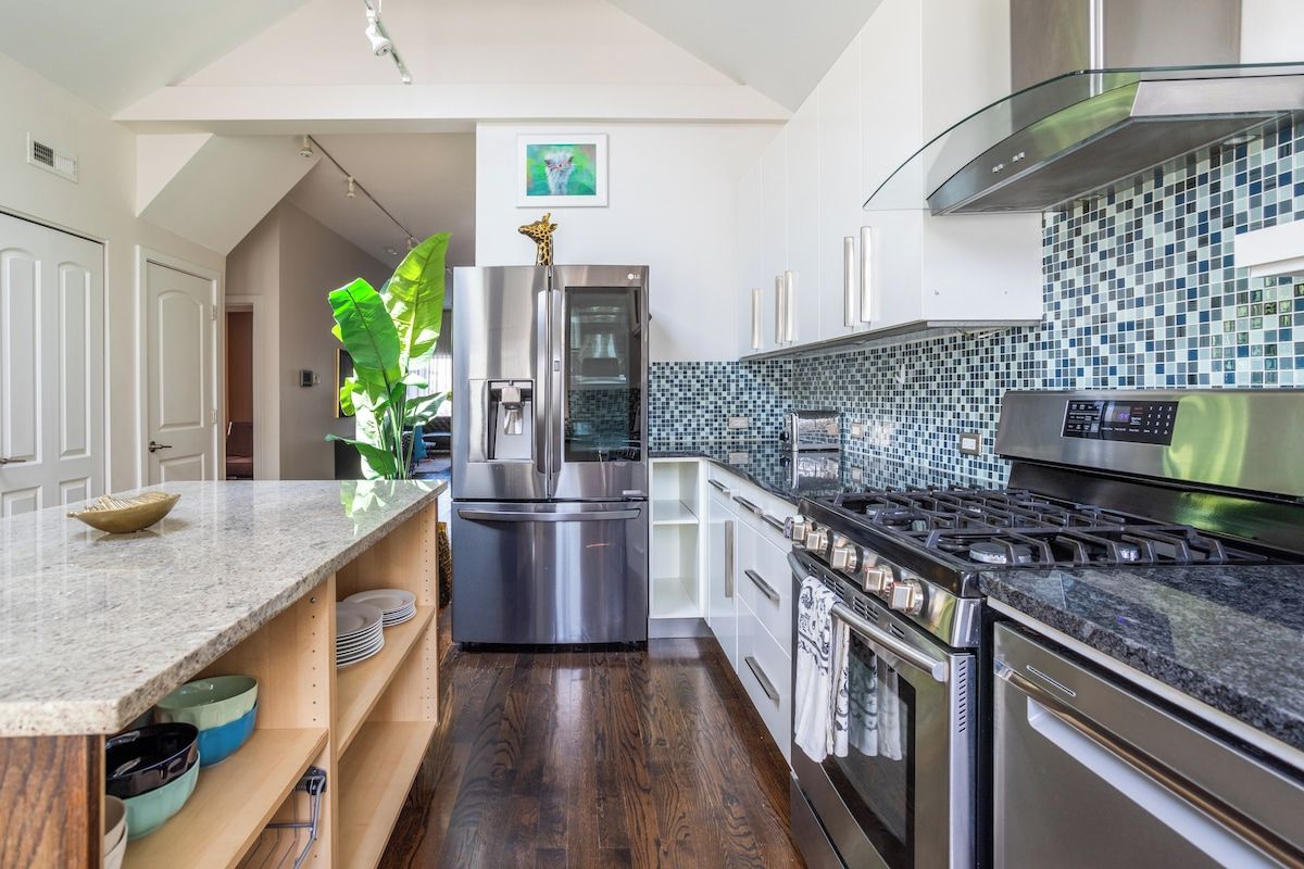 Een moderne keuken met roestvrijstalen apparatuur, een betegelde spatwand en een houten vloer.