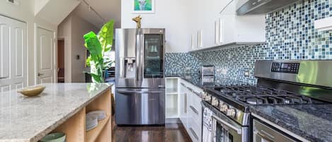 A modern kitchen with stainless steel appliances, a tiled backsplash, and a wooden floor.