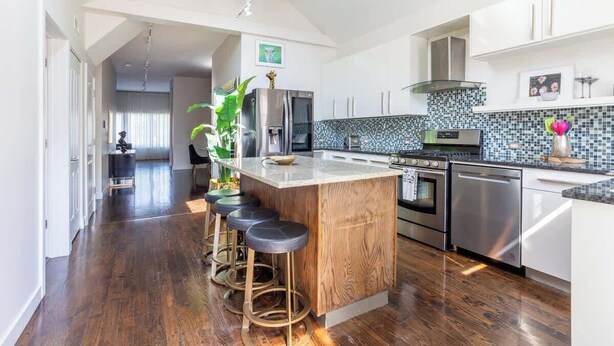 A modern kitchen with a central island, bar stools, stainless steel appliances, and a tiled backsplash. - Duplex 3 Bed 2 Bath Apt Steps from Lincoln Square (Chicago)