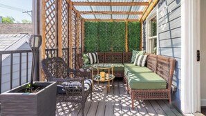 A covered outdoor seating area with wicker furniture, a green cushioned sofa, and a small table. - Duplex 3 Bed 2 Bath Apt Steps from Lincoln Square (Chicago)
