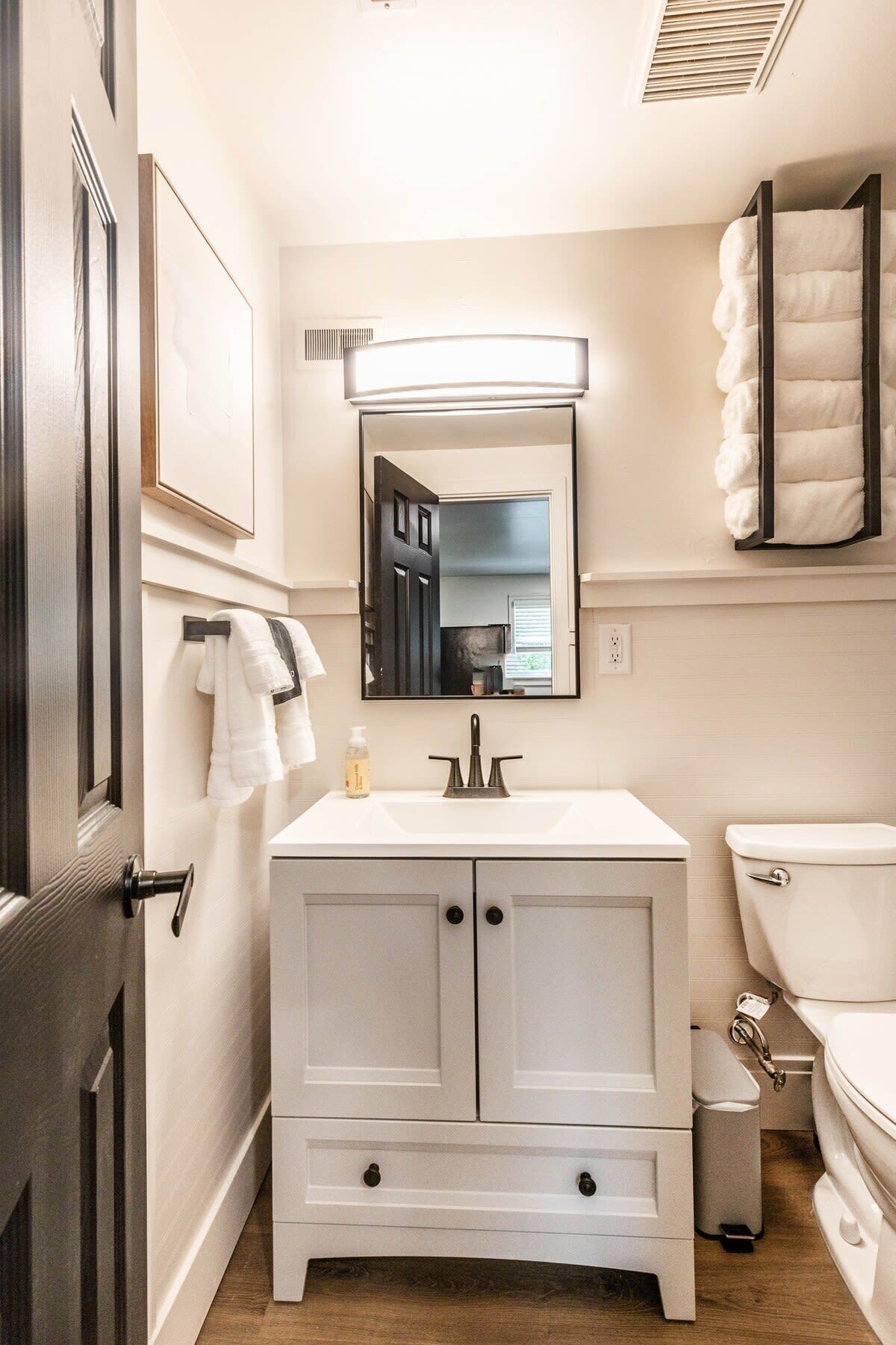 A bathroom with a white vanity, a mirror, a toilet, and a towel rack.