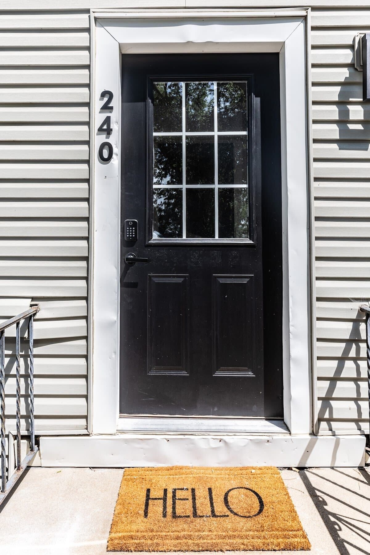 A black door with a window, a 'HELLO' mat, and the number '240' on the wall.