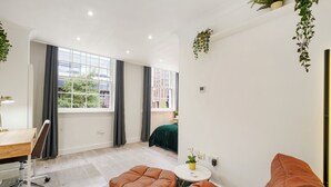 Ein modernes Zimmer mit einem großen Fenster, einem Schreibtisch, zwei braunen Sofas und einem kleinen Tisch mit einer Pflanze.