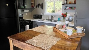 Eine Küche mit einem Holztisch, Barhocker, einem schwarzen Kühlschrank, einem Herd, einer Spüle und einem Fenster mit Vorhängen.
