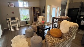 Ein Wohnzimmer mit einer Couch, Hocker, einem Couchtisch, einem Bücherregal und einem Essbereich mit Tisch und Stühlen.