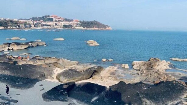 Un paisaje costero con grandes rocas y una vista distante de edificios en una colina.