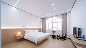 Una habitación de hotel moderna con una cama grande, una mesita de noche con lámpara, televisión y un amplio ventanal con cortinas.