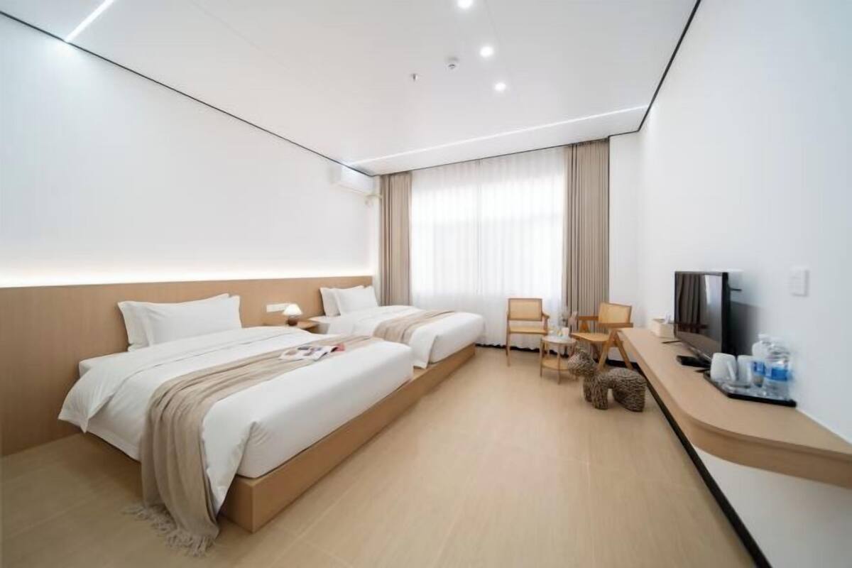 Een moderne hotelkamer met een bed, twee stoelen, een bureau, een televisie en een groot raam met gordijnen.