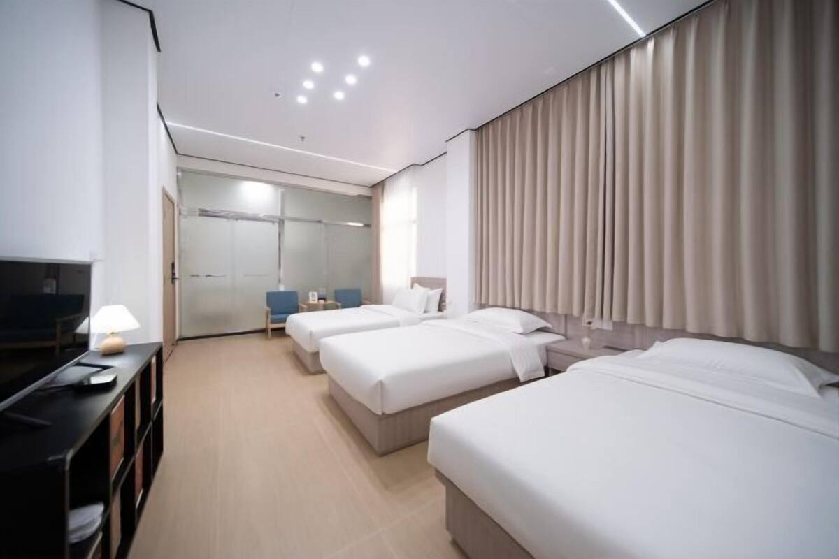 Een hotelkamer met drie bedden, een bureau met een lamp, een televisie en een badkamer met een glazen deur.