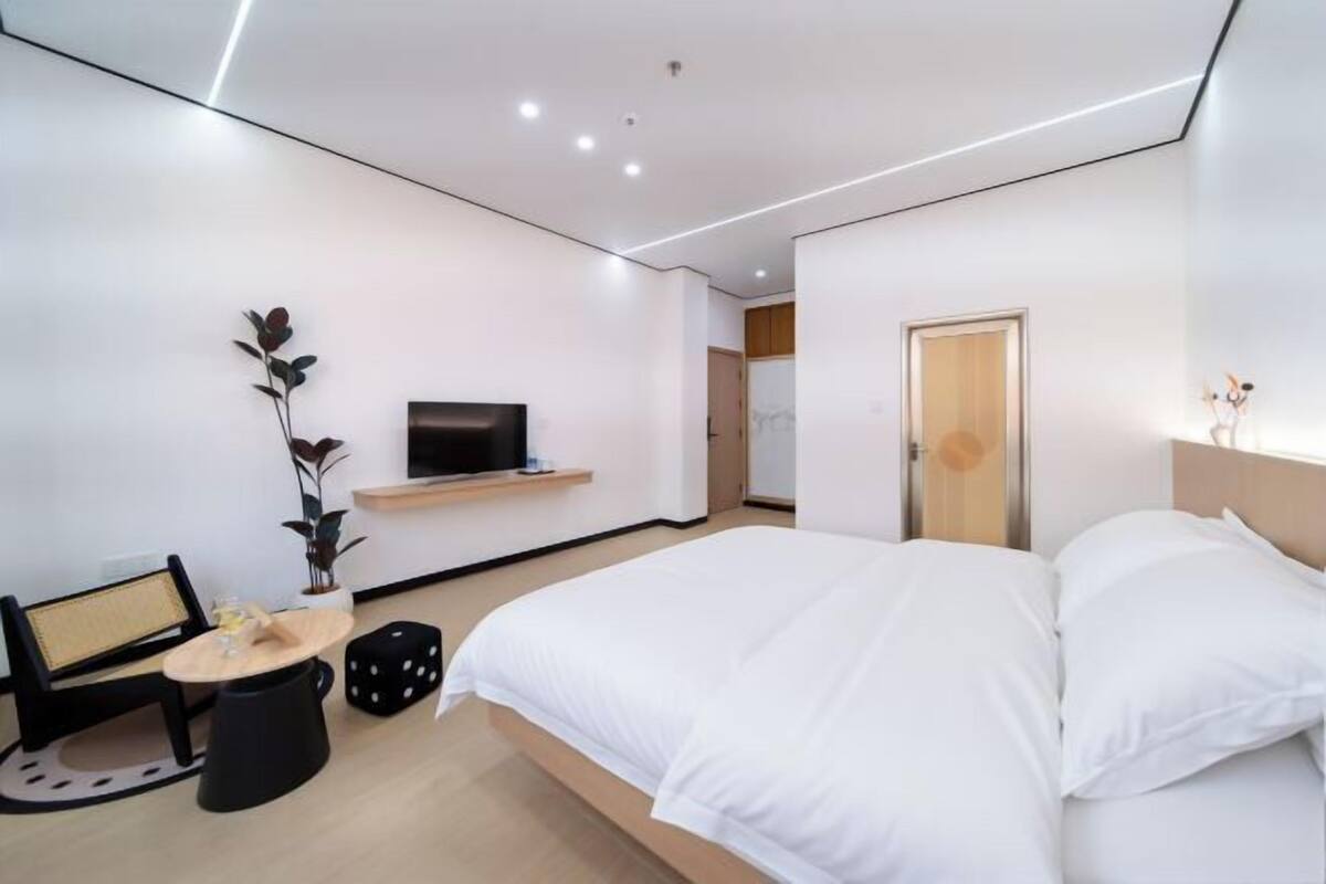 Een moderne hotelkamer met een bed, een televisie, een tafeltje en een plant.