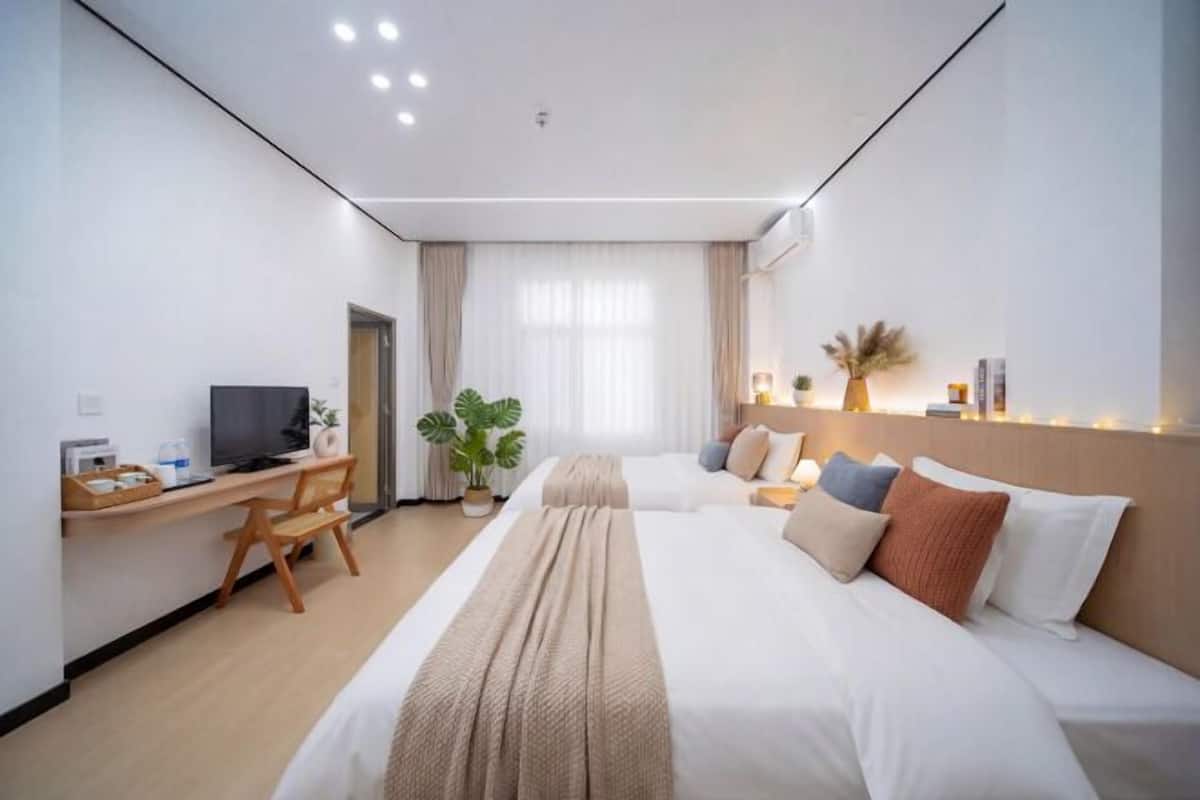 Een hotelkamer met twee bedden, een bureau, een televisie, een potplant en een raam met gordijnen.