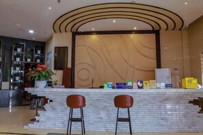 A reception area with a marble counter, two bar stools, a potted plant, and a wall with a wave-like design. - Huamei Business Hotel (Tongxiang)