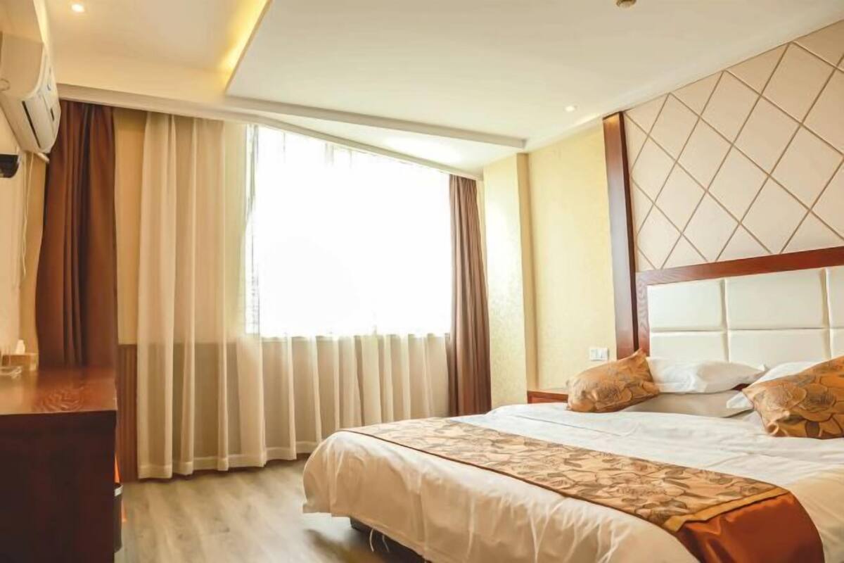 Ein Hotelzimmer mit einem großen Bett, einem hölzernen Kopfteil und einem Fenster mit Vorhängen.
