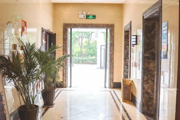A hotel lobby with a marble floor, a reception desk, and a large potted plant.