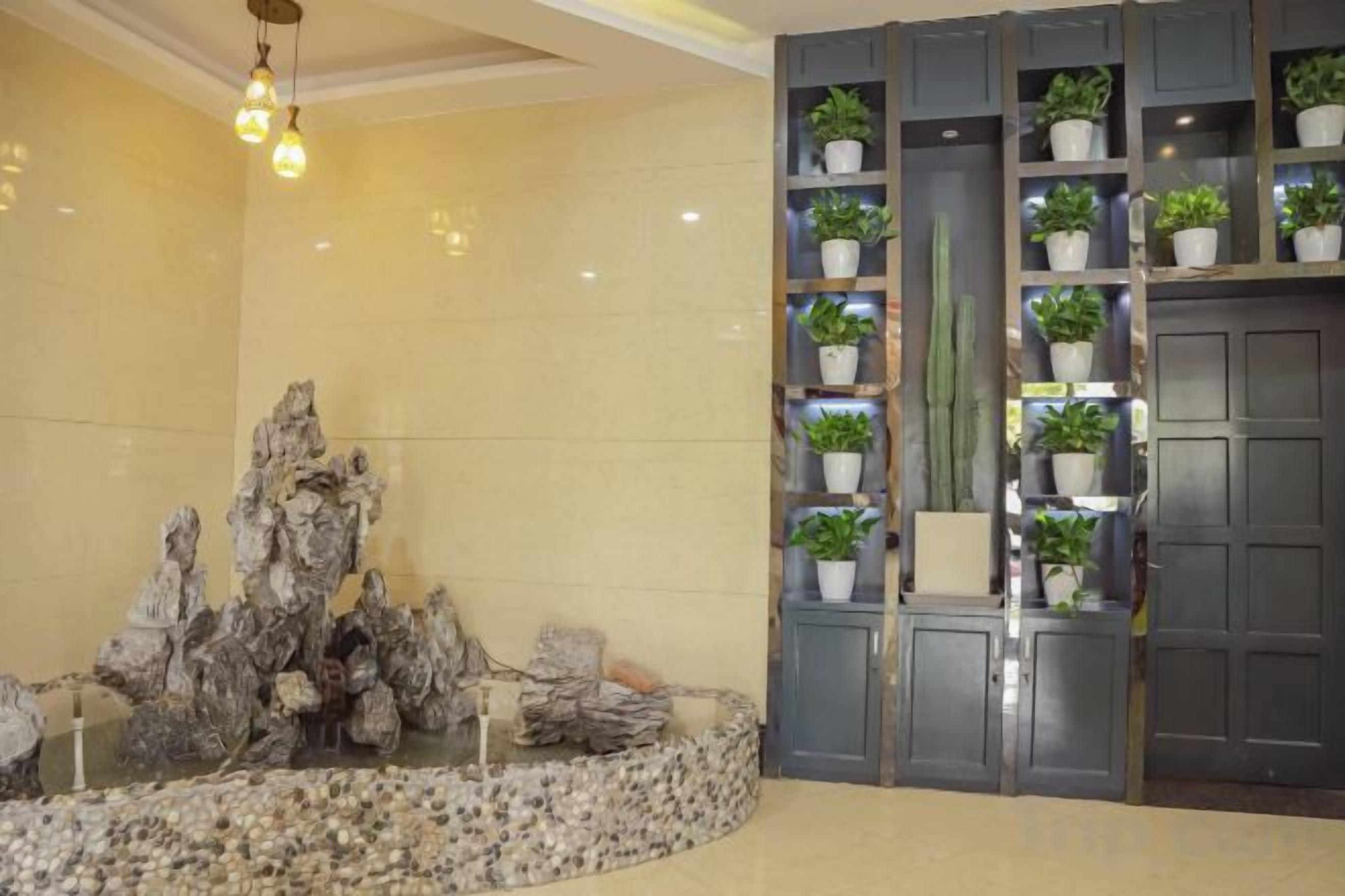 Un vestíbulo con una formación rocosa como pieza central, una estantería con plantas en macetas y una puerta.