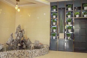 A lobby with a rock formation centerpiece, a potted plant shelf, and a door. - Huamei Business Hotel (Tongxiang)
