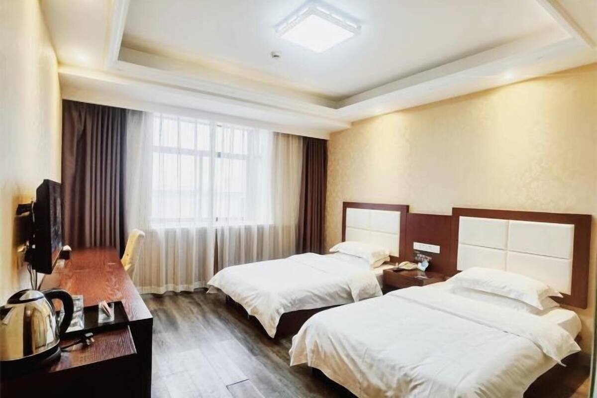 Ein Hotelzimmer mit zwei Betten, einem Schreibtisch, einem Sessel, einem Fernseher und einem Fenster mit Vorhängen.