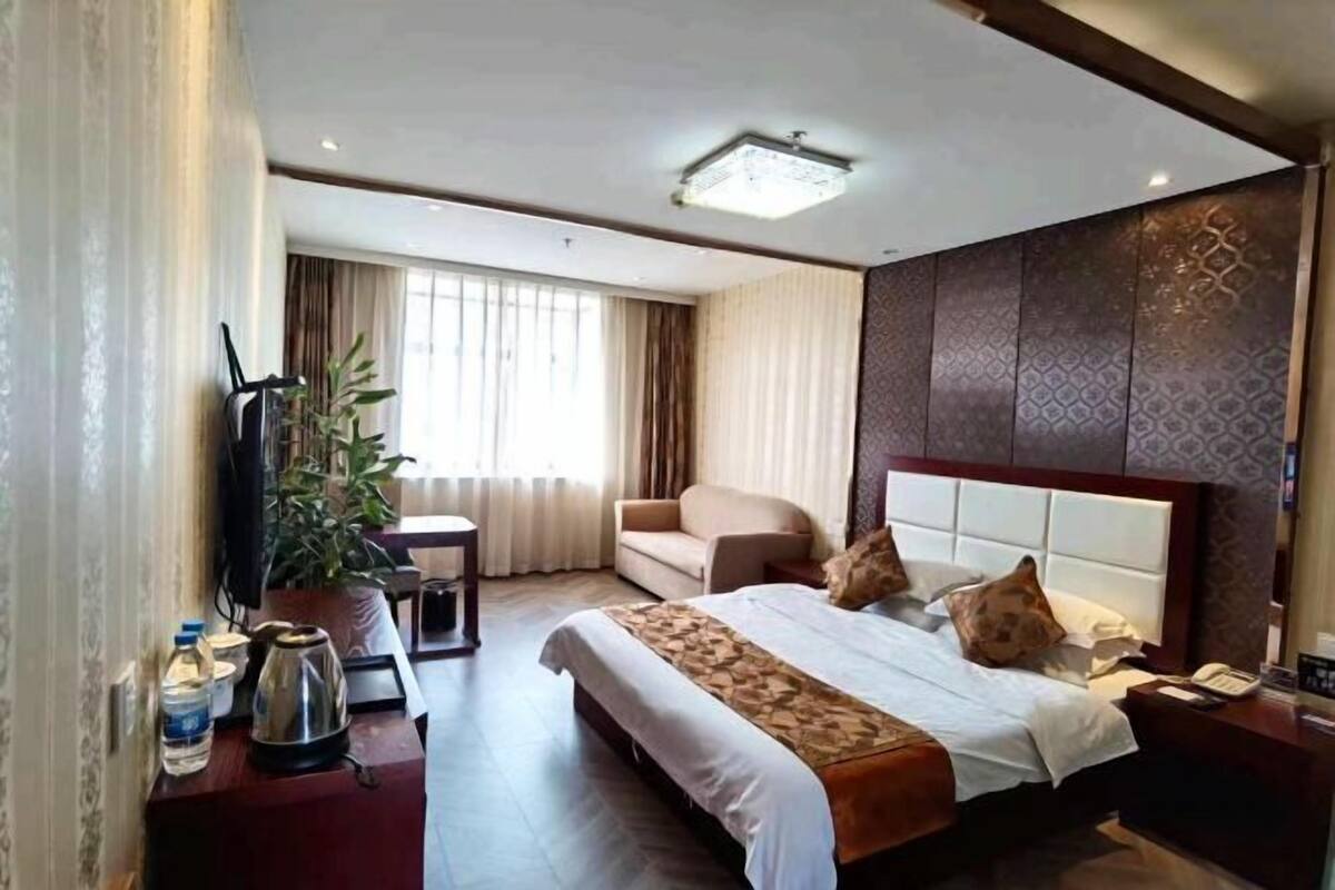 Ein Hotelzimmer mit Bett, Sofa, Schreibtisch, einer Pflanze und einem Fenster mit Vorhängen.