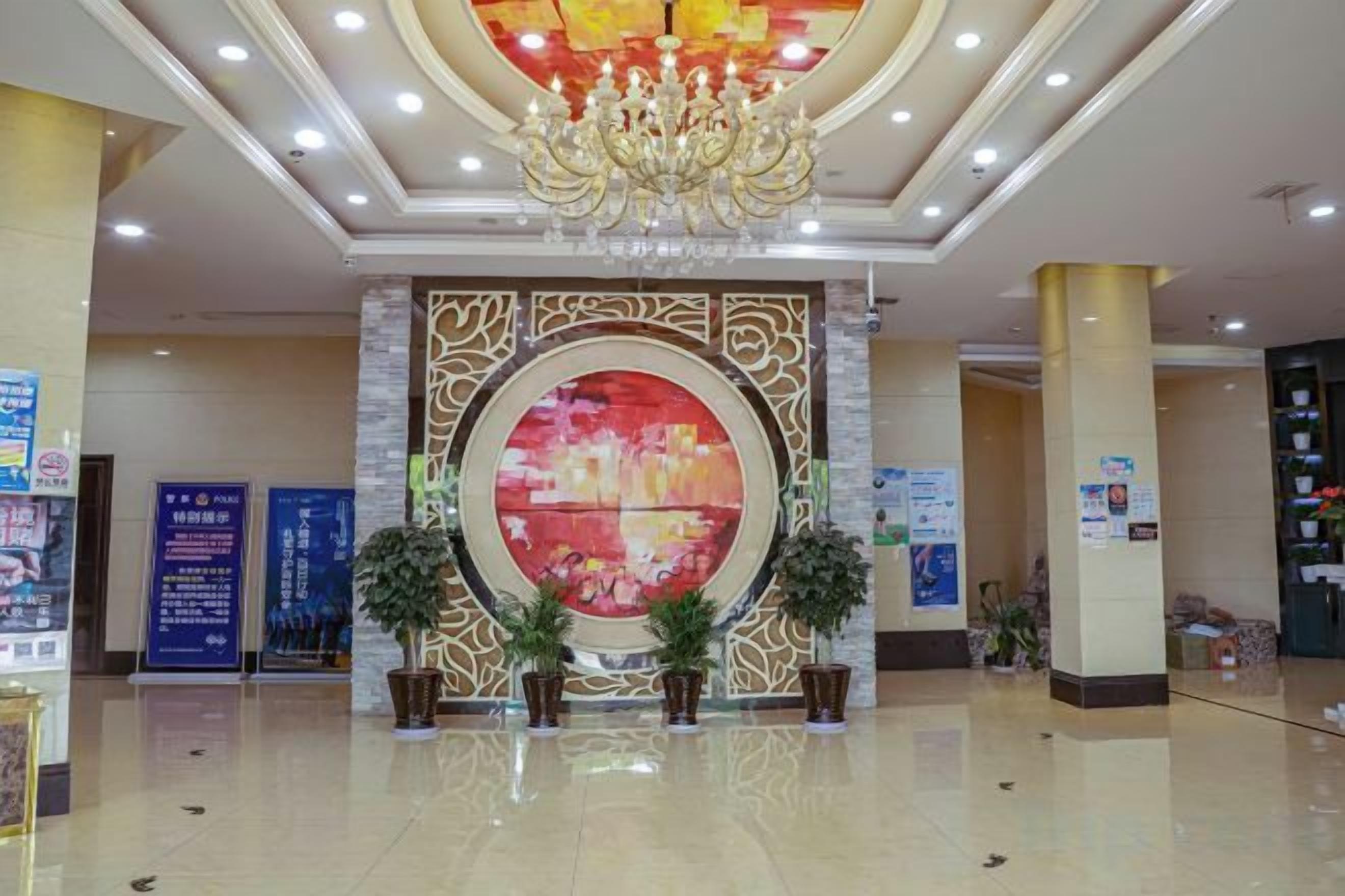 A lobby with a large circular artwork, a chandelier, and potted plants.